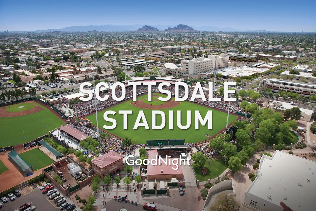 A vibrant, action-filled baseball stadium scene with a crowd of spectators, mountain backdrops, and classic stadium architecture. The energy of fans watching a live baseball game is palpable, evoking the excitement of Scottsdale’s Spring Training events.