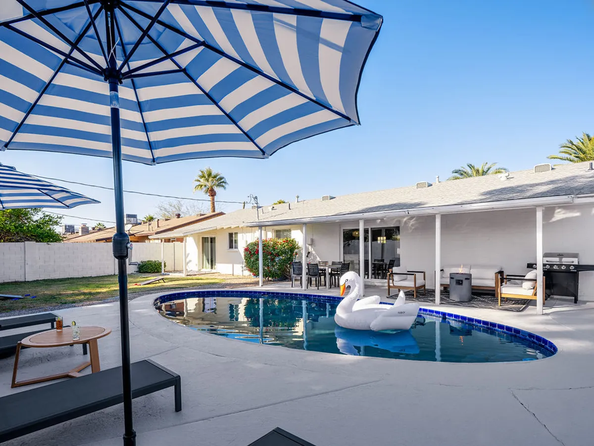 The hero image showcases a sparkling pool framed by cheerful striped umbrellas, a whimsical swan float, and stylish lawn furniture, all set against a warm Arizona sunset. The scene radiates relaxation and social energy, with inviting spaces for swimming, sunbathing, grilling, and gathering with friends or family.