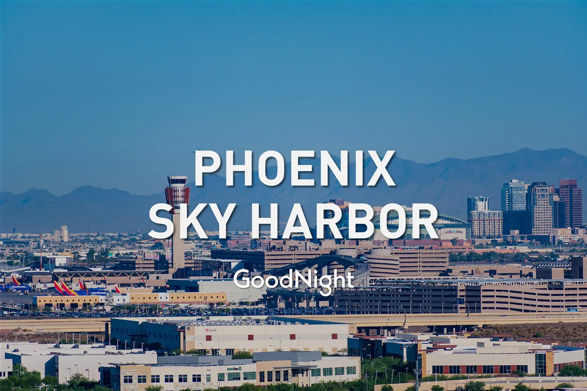 A panoramic exterior view that captures Phoenix Sky Harbor Airport in the foreground with the Downtown Phoenix skyline and surrounding mountains as a dramatic backdrop. The scene pulses with the energy of travel, business, and city life.